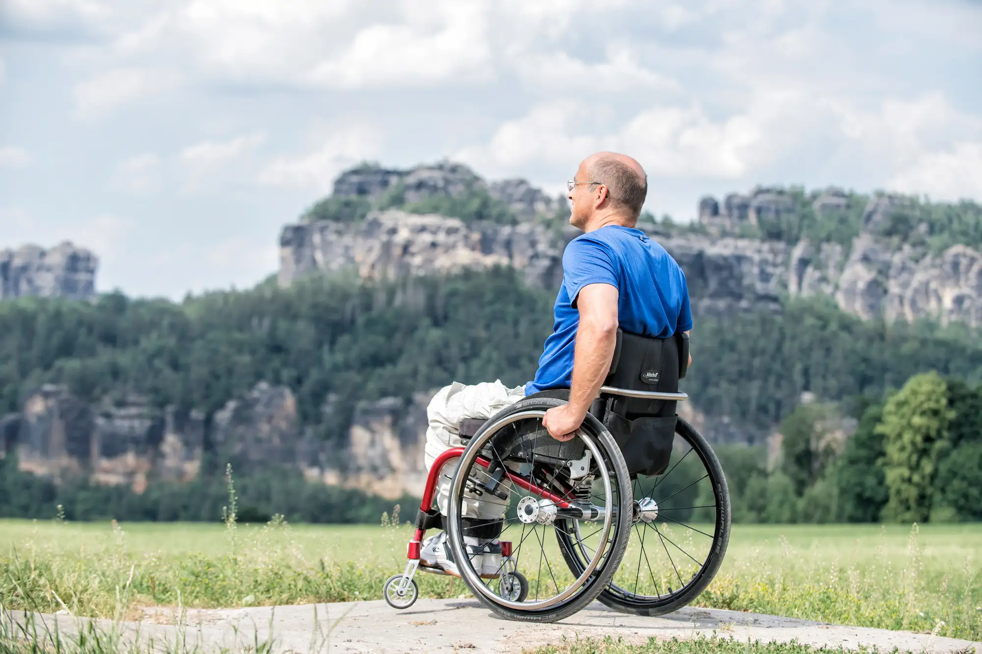 Der zertifizierte Nationalparkführer Veit Riffer, Rollifahrer und Freizeitsportler, hat viele Touren für Rollsuhlfahrer getestet. Im Bild ist er mit dem Felsenpanorama der Schrammsteine im Hintergrund zu sehen.