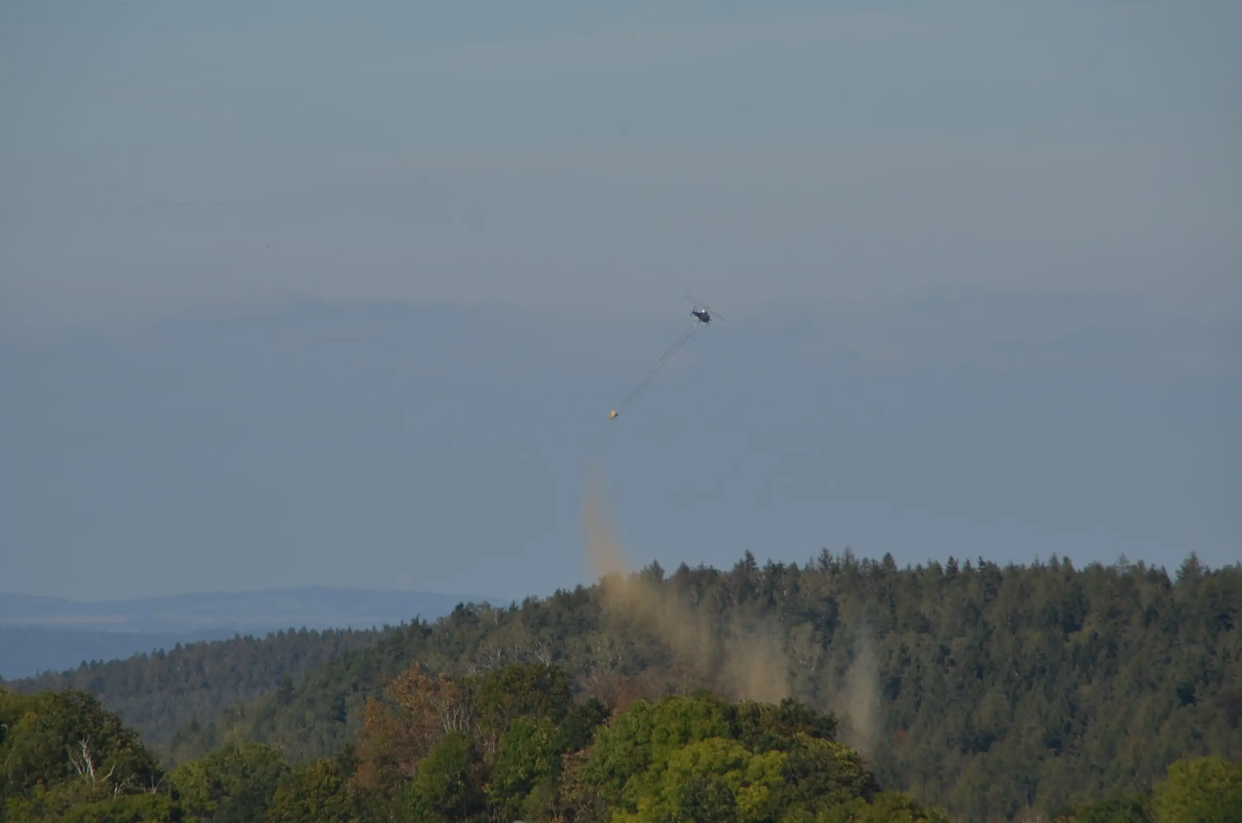 Ein Hubschrauber lässt gemahlenes Dolomitgestein zur Waldkalkung über einen bewaldeten Hügel ab