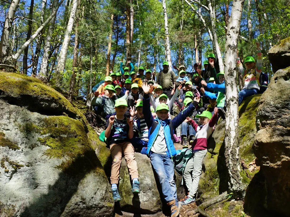 Sächsisch-böhmische Junior Ranger sitzen gemeinsam zwischen zwei Felsen im Wald und haben viel Freude an gemeinsamen Naturerlebnissen.