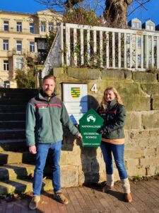 Christian Starke übergibt mit einem Nationalparkschild symbolisch die Leitung für den Fachbereich Naturschutz, Gebietsentwicklung und Forschung an Astrid Scharf. Sie arbeitete bereits acht Monate in diesem Bereich, bevor sie nun die Leitung übernahm. Starke ist seit vergangenem Jahr Leiter des Wildnisgebiets auf dem ehemaligen Truppenübungsplatz Königsbrück. Foto: H. Mayr